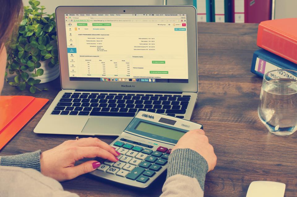 Hands using a calculator next to a laptop showing a budget spreadsheet